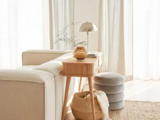 Gemütliches Wohnzimmer mit beigem Sofa, Holztisch, Lampe und Korb. Die helle Atmosphäre vermittelt das Gefühl von Hygge Bedeutung: Wohlbefinden und Gemütlichkeit.