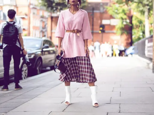Ein Midirock kombiniert mit einem rosa Pullover und weißen Stiefeln – ein lässiger Sommer-Look auf der Straße.
