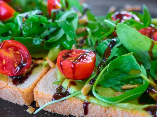 Leckere Bruschetta mit Avocado, Tomaten und Rucola, beträufelt mit Balsamico. So lassen sich Balsamico-Flecken entfernen: schnell handeln!