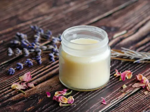 Ein Glas selbstgemachte Handcreme mit Lavendel und Rosenblüten auf Holzuntergrund.