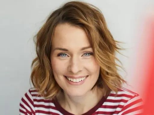 Eine Frau mit schulterlangen, welligen Haaren und einem strahlenden Lächeln. Diese Frisuren 2026 halblang sind modern und schmeichelhaft.