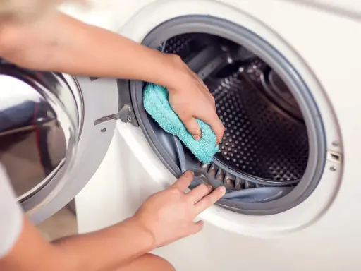 Hände reinigen die Gummidichtung der Waschmaschine mit einem blauen Tuch. Hausmittel helfen, die Waschmaschine zu reinigen und Gerüche zu vermeiden.