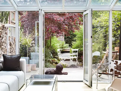 Gemütliche Wintergarten einrichten Ideen: Hund liegt auf Holzterrasse vor Garten mit rotem Ahornbaum und weißem Mobiliar.