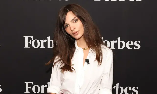 Emily Ratajkowski mit langen, gestuften Haaren und einem weißen Hemd vor einem Forbes-Banner.