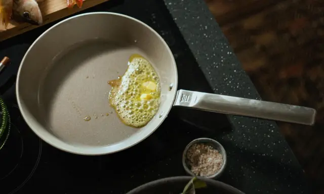 Eine beschichtete Pfanne reinigen: Butter schmilzt und blubbert, bereit für den Fisch.