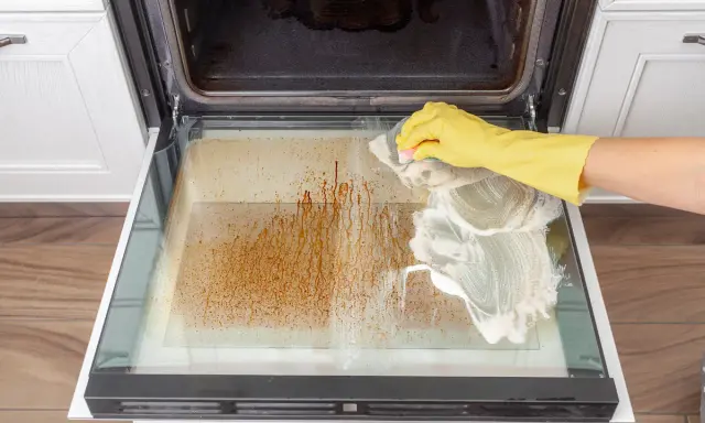 Gelbe Handschuhe reinigen mit Schaum die stark verschmutzte Backofentür.