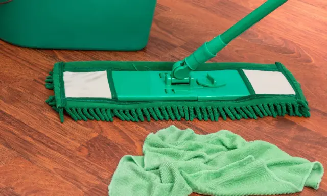 Grüner Wischmopp und Eimer auf Holzfußboden, bereit für die Reinigung. Wie oft wischen Sie Ihren Boden?