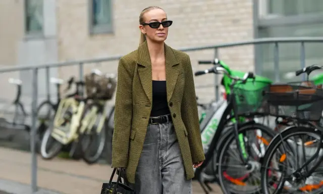 Stilvolle Frau mit Sonnenbrille und kariertem Blazer, die zeigt, wie man graue Jeans kombiniert.