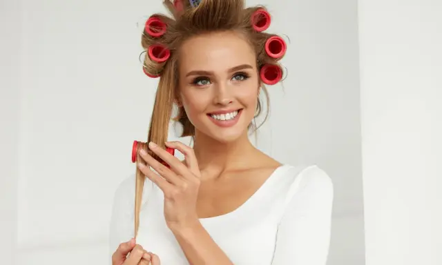 Lächelnde Frau mit roten Wicklern im Haar, die sich Locken macht.