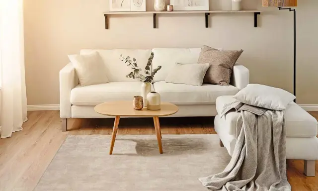 Ein helles Wohnzimmer mit weißem Sofa, Holztisch und Teppich. Perfekt für minimalistisch wohnen.
