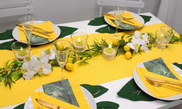 Sommerliche tischdeko mit zitronen, Orchideen und grünen Blättern. Kerzen in Gläsern sorgen für stimmungsvolles Licht.
