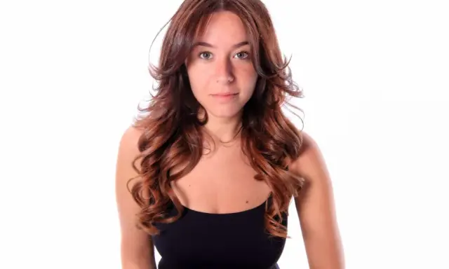 Frau mit langen, welligen Haaren im Butterfly Cut, die einen schwarzen Tanktop trägt.