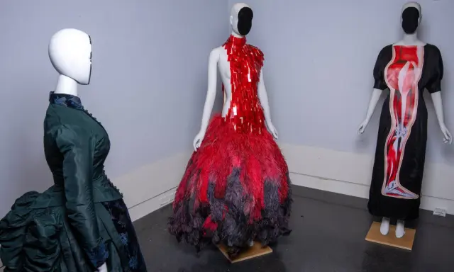 Drei Schaufensterpuppen präsentieren extravagante Kleider, die an das Met Gala Thema erinnern: eines in Grün im viktorianischen Stil, eines in Rot mit Federn und eines mit anatomischem Druck.