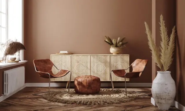 Ein gemütliches Wohnzimmer im Boho-Stil mit zwei Ledersesseln, einem runden Teppich, einem Sideboard und Trockenblumen.