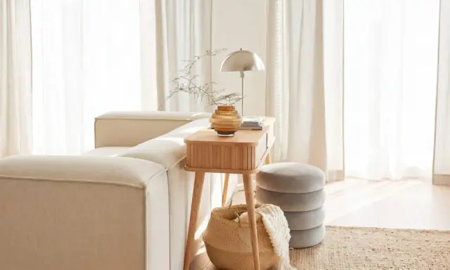 Gemütliches Wohnzimmer mit beigem Sofa, Holztisch, Lampe und Korb. Die helle Atmosphäre vermittelt das Gefühl von Hygge Bedeutung: Wohlbefinden und Gemütlichkeit.
