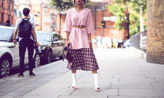 Ein Midirock kombiniert mit einem rosa Pullover und weißen Stiefeln – ein lässiger Sommer-Look auf der Straße.