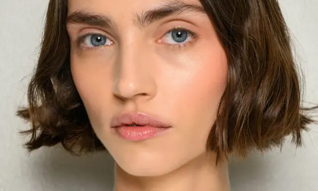 Nahaufnahme einer Frau mit einem kurzen Bob-Haarschnitt, blauen Augen und rosafarbenen Wangen.