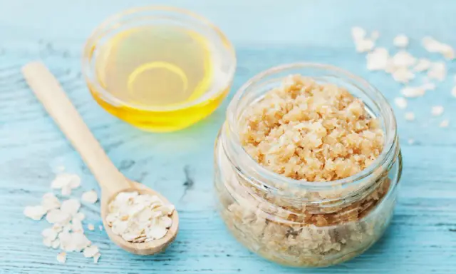 Zutaten für ein **Gesichtspeeling selber machen**: Haferflocken auf einem Holzlöffel, ein Glas mit Peeling und eine Schale mit Öl.
