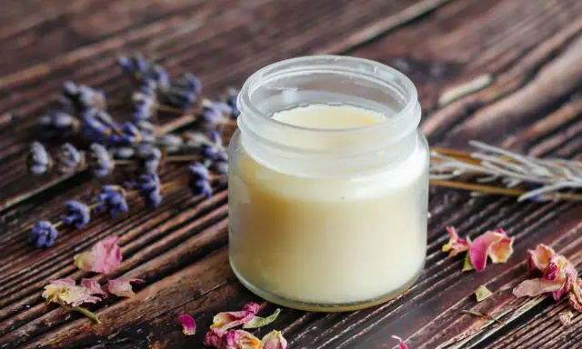 Ein Glas selbstgemachte Handcreme mit Lavendel und Rosenblüten auf Holzuntergrund.