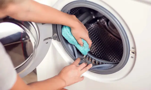 Hände reinigen die Gummidichtung der Waschmaschine mit einem blauen Tuch. Hausmittel helfen, die Waschmaschine zu reinigen und Gerüche zu vermeiden.