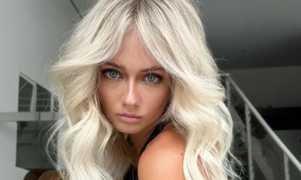 Blonde Frau mit voluminöser blowout frisur und blauen Augen blickt ernst in die Kamera.