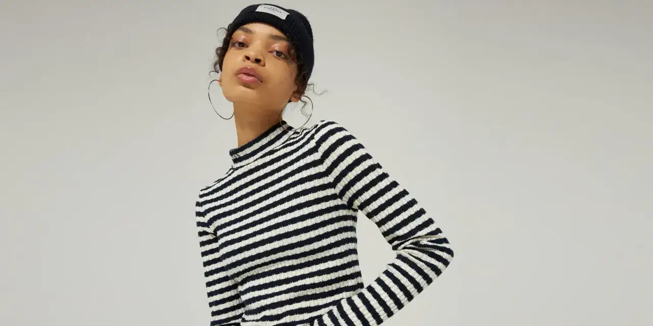 Ein junges Model im Streifen-Rollkragenpullover und Beanie-M&uuml;tze, mit gro&szlig;en Creolen, verk&ouml;rpert den l&auml;ssigen VSCO Girl-Look.
