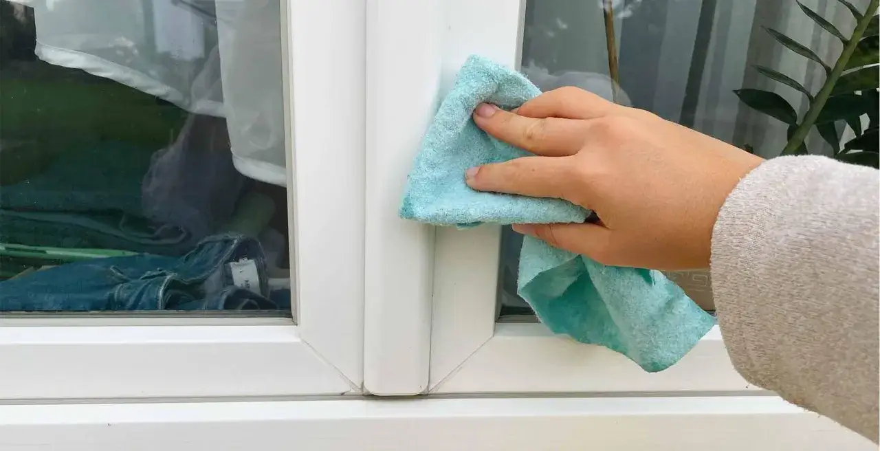 Hand reinigt mit blauem Tuch den weißen Kunststoff Fensterrahmen.