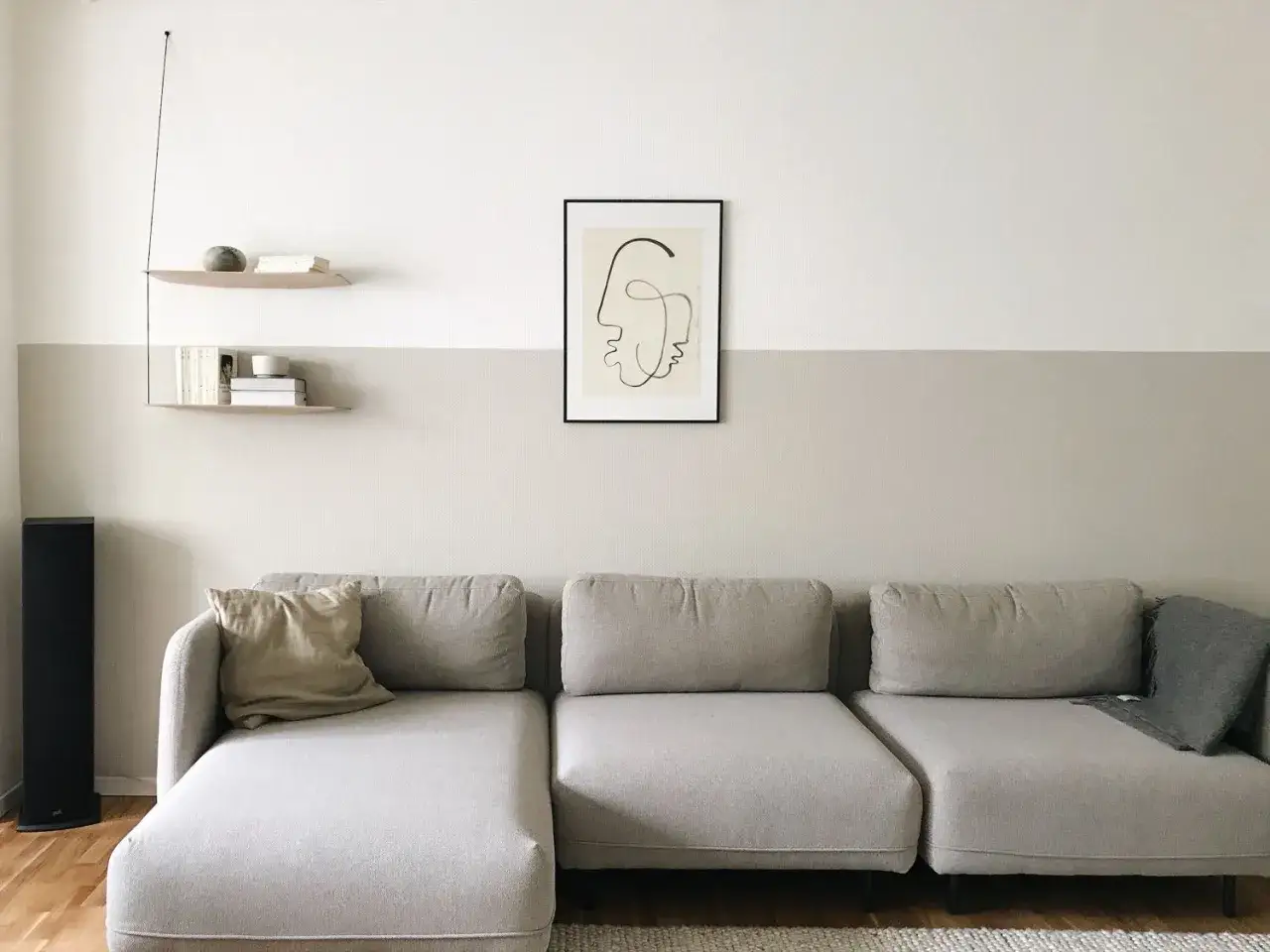 Gemütliches Wohnzimmer mit zweifarbig gestrichener Wand, einem Sofa und minimalistischer Deko. Der Rand zwischen den Farben ist sauber gezogen.