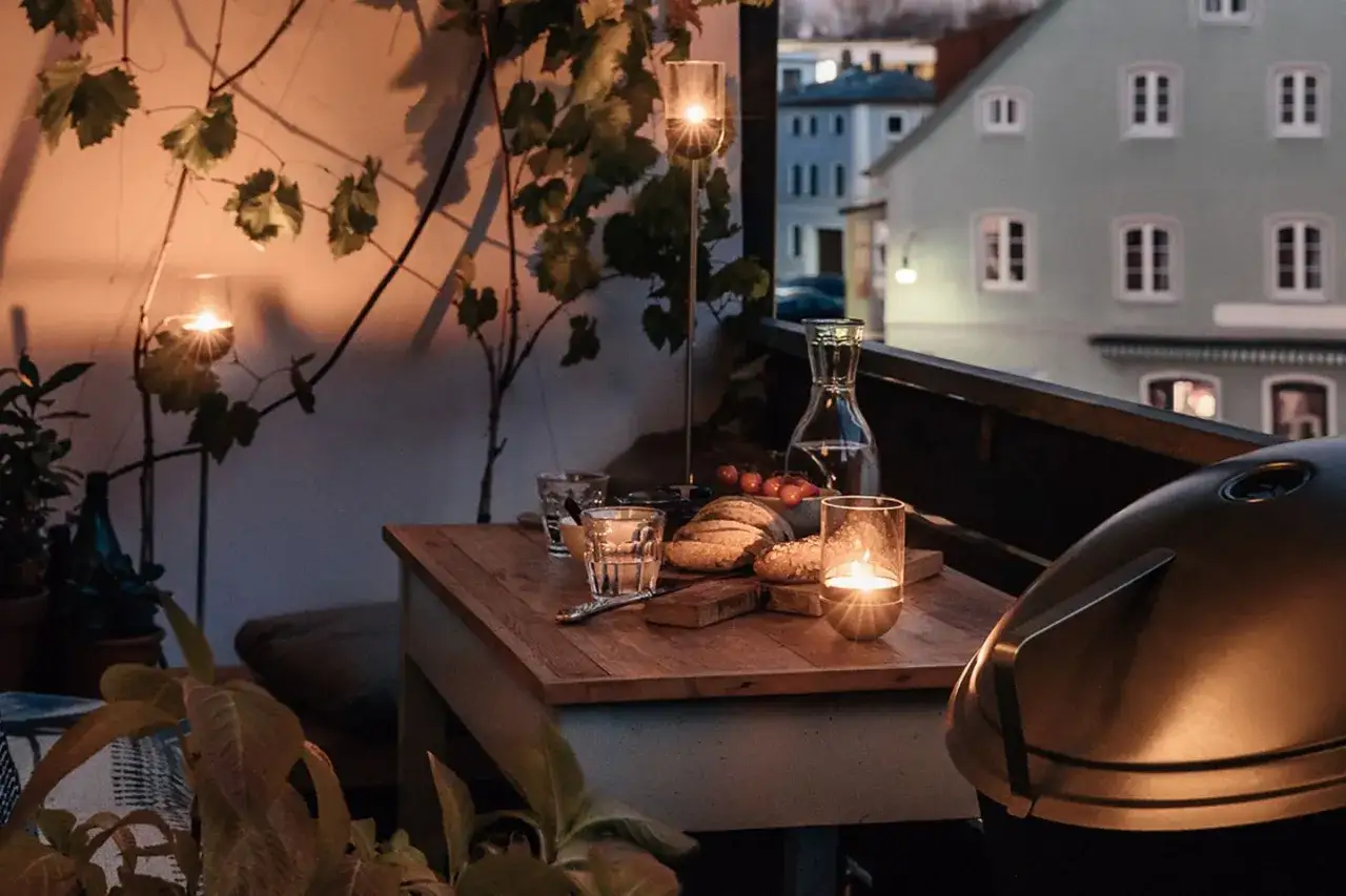 Gem&uuml;tliche Balkon Ideen: Kerzenlicht, Brot und Wein auf einem Holztisch, daneben ein Grill.