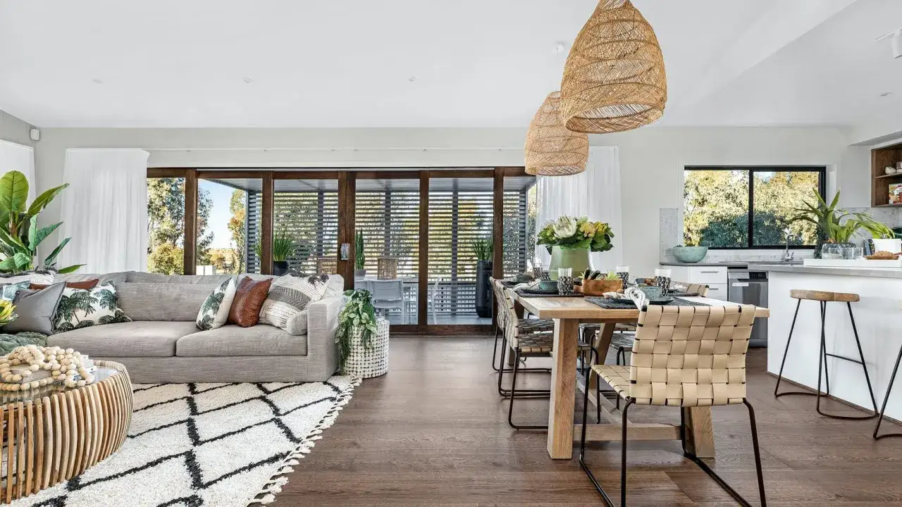Ein helles, offenes Wohn-Esszimmer mit gemütlicher Couch, Esstisch und moderner Küche. Große Fensterfronten lassen viel Licht herein.