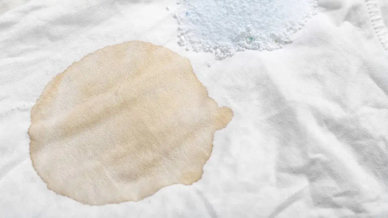 Brauner Fleck auf wei&szlig;em Stoff, dane ein Haufen Waschpulver. So lassen sich Balsamico-Flecken entfernen.