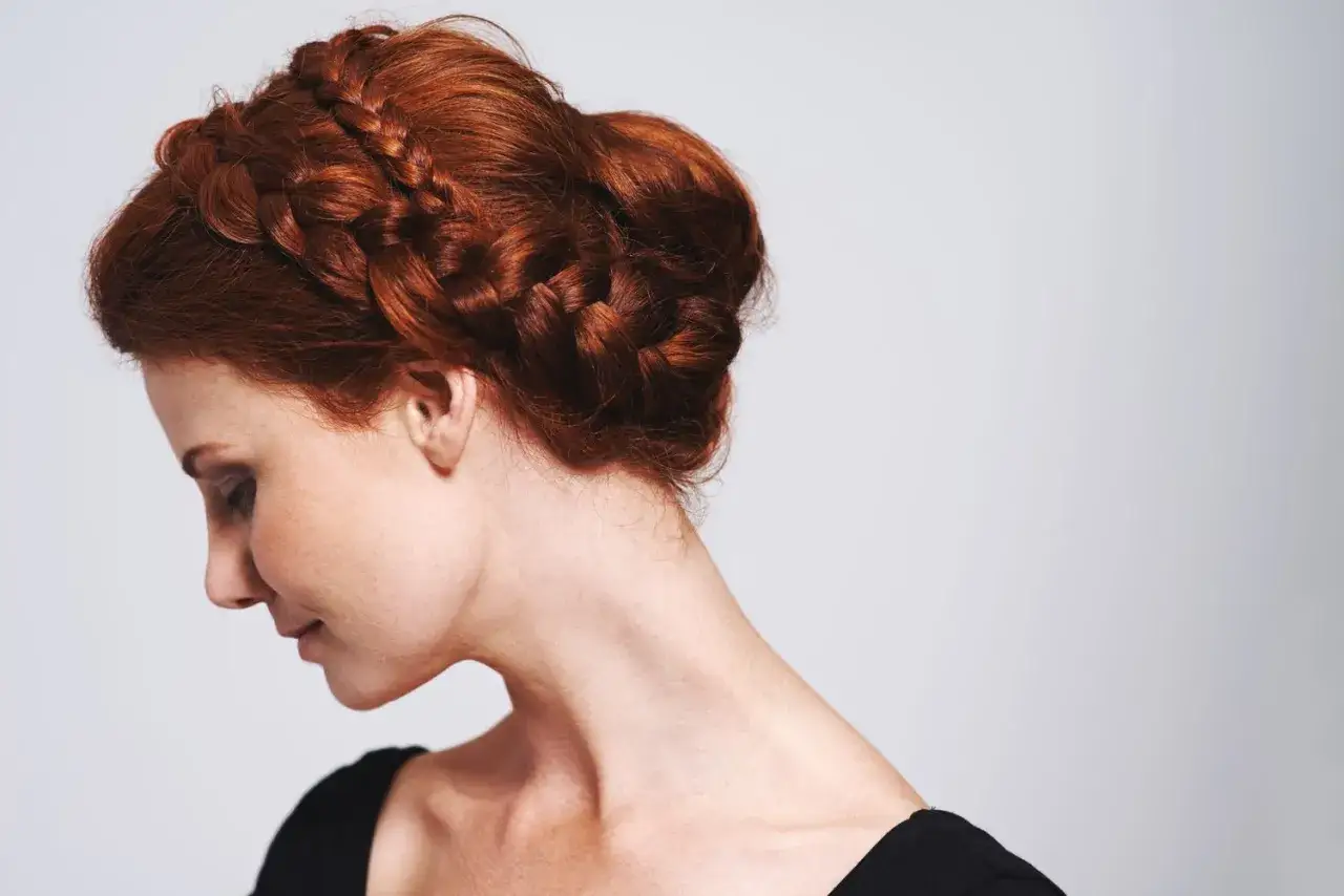 Eine Frau mit roten Haaren trägt eine elegante Hochsteckfrisur mittellang, geflochten und hochgesteckt.