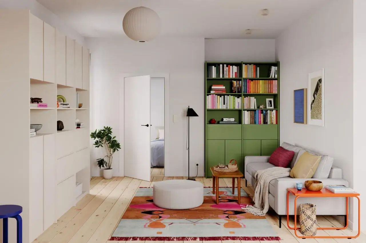 Ein gemütliches kleines Wohnzimmer einrichten mit viel Stauraum durch weiße Schränke, einer grünen Bücherwand und einem farbenfrohen Teppich.