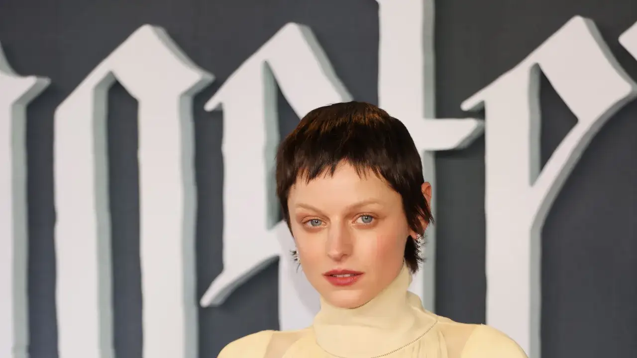 Frau mit einem frechen Pixie-Cut und einem gelben Kleid, das auf einem roten Teppich posiert.