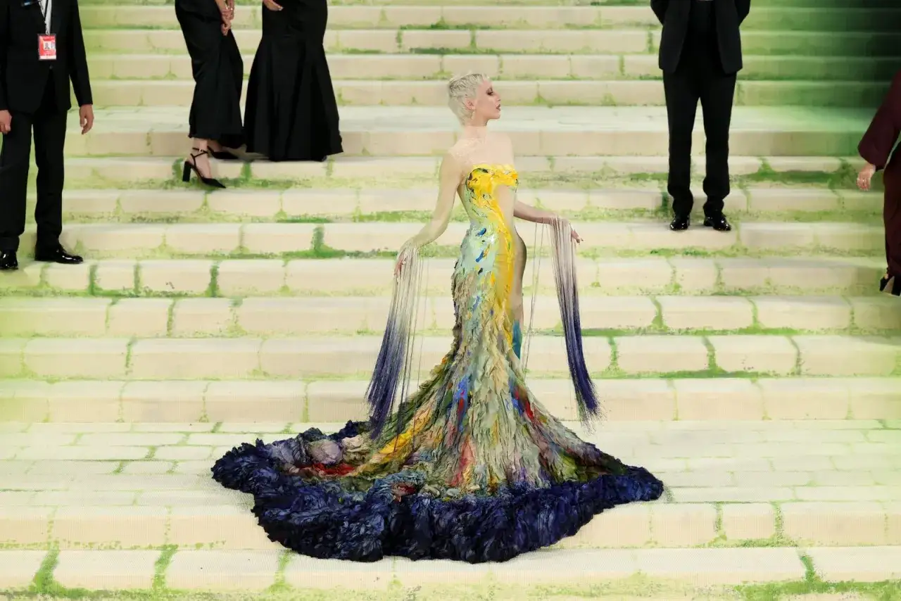 Ein farbenprächtiges Kleid, inspiriert vom Met Gala Thema, entfaltet sich wie ein Pfau auf einer Treppe.