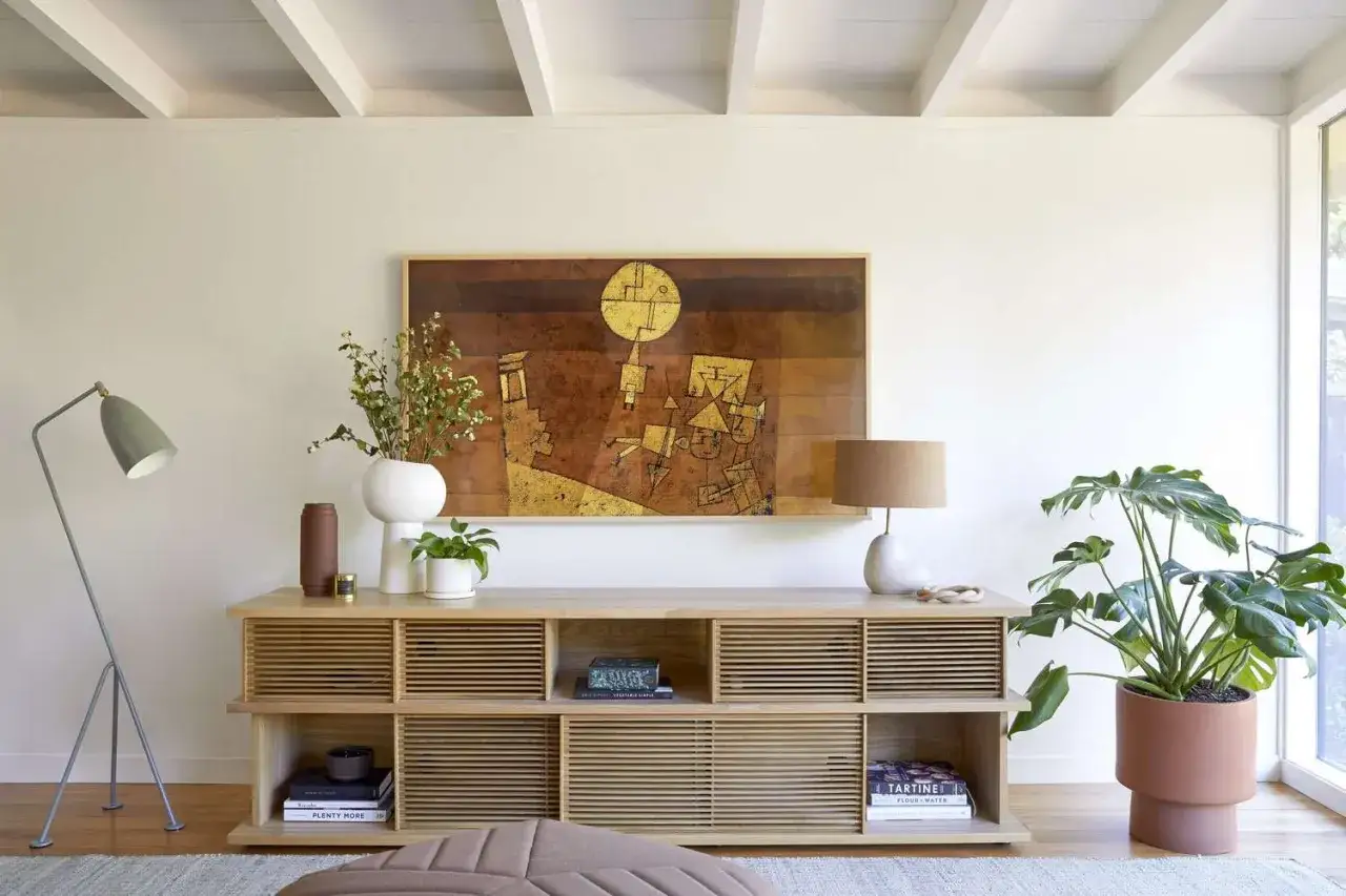 Ein helles Sideboard wird mit Vasen, Pflanzen und B&uuml;chern dekoriert. Ein abstraktes Gem&auml;lde h&auml;ngt dar&uuml;ber.