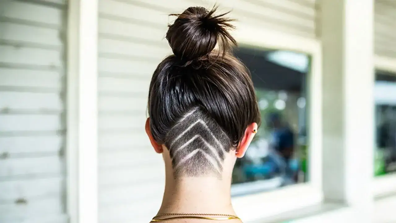Frauen mit einem auffälligen Undercut, der in einem Pfeilmuster rasiert ist. Der obere Teil des Haares ist zu einem Dutt hochgesteckt.