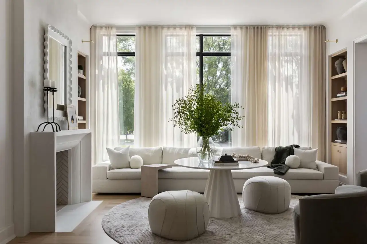 Ein helles Wohnzimmer mit einem wei&szlig;en Sofa, runden Poufs und einem runden Tisch. Minimalistisch wohnen wird durch dezente Farben und klare Linien unterstrichen.