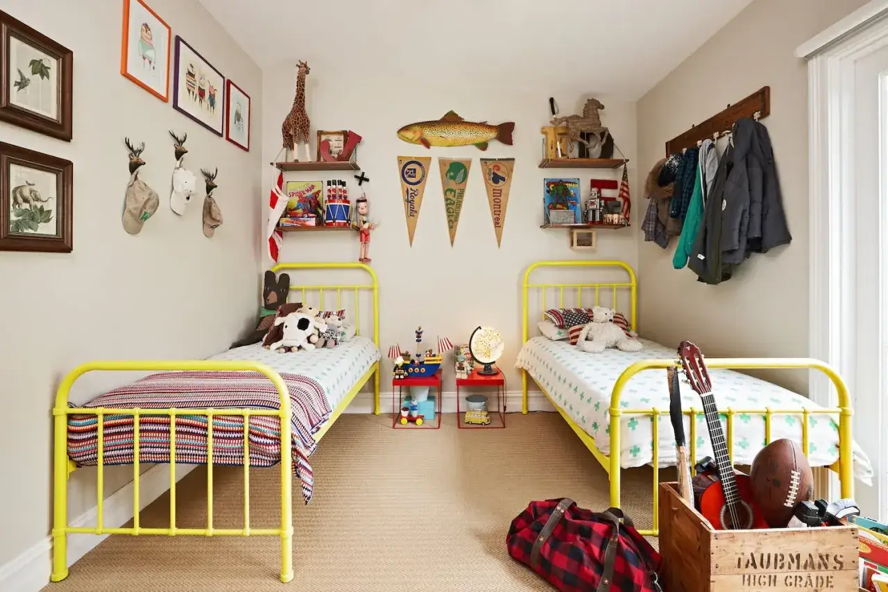 Zwei gelbe Betten in einem Kinderzimmer mit Spielzeug, Giraffenfigur und Wanddeko. Tolle geschwisterzimmer ideen für Abenteuer!