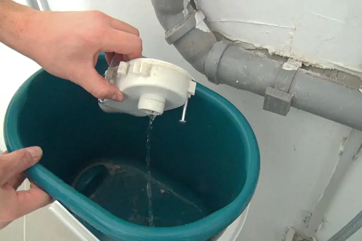 Wasser läuft aus dem Filter einer Waschmaschine in einen Eimer. Der Grund, warum die Waschmaschine nach Kanal stinkt, ist oft ein verstopfter oder verschmutzter Filter.