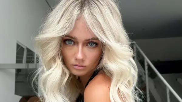 Blonde Frau mit voluminöser blowout frisur und blauen Augen blickt ernst in die Kamera.