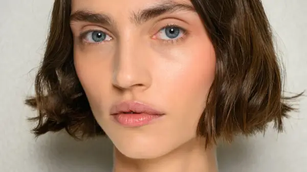 Nahaufnahme einer Frau mit einem kurzen Bob-Haarschnitt, blauen Augen und rosafarbenen Wangen.