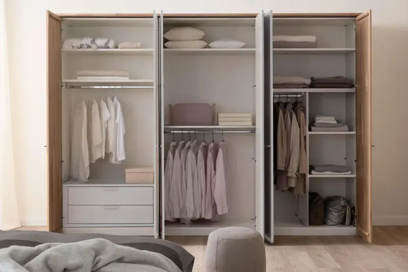 Ein offener Kleiderschrank, bereit zum Ausmisten. Ordentlich sortierte Kleidung auf Kleiderbügeln und gefaltete Textilien auf den Regalen.