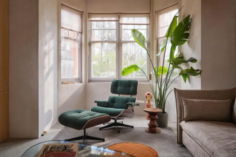 Gemütliche Ecke im midcentury stil mit einem grünen Cord-Sessel und Hocker, daneben eine große Zimmerpflanze und ein Beistelltisch.