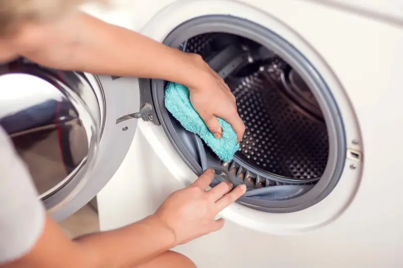 Hände reinigen die Gummidichtung der Waschmaschine mit einem blauen Tuch. Hausmittel helfen, die Waschmaschine zu reinigen und Gerüche zu vermeiden.