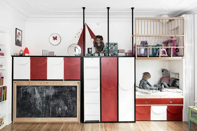 Kreative geschwisterzimmer ideen: Kinder spielen in einem bunten Zimmer mit Hochbetten, Rutsche und Tafel.